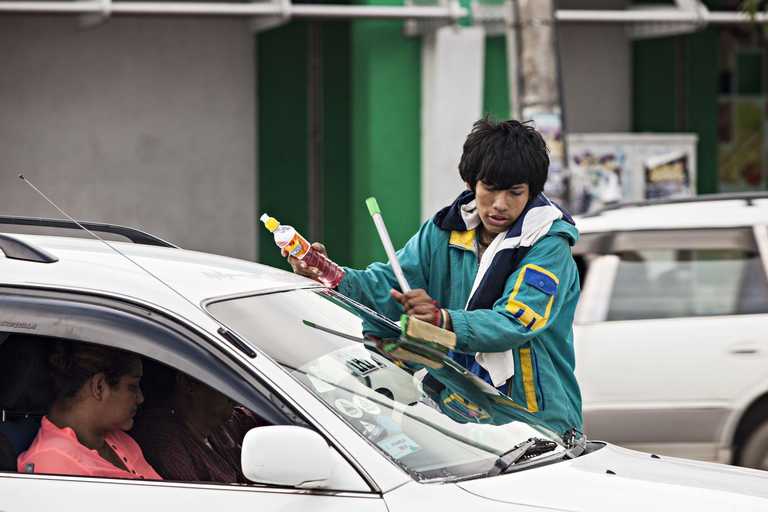 Ein Junge putzt die Scheiben eines Autos