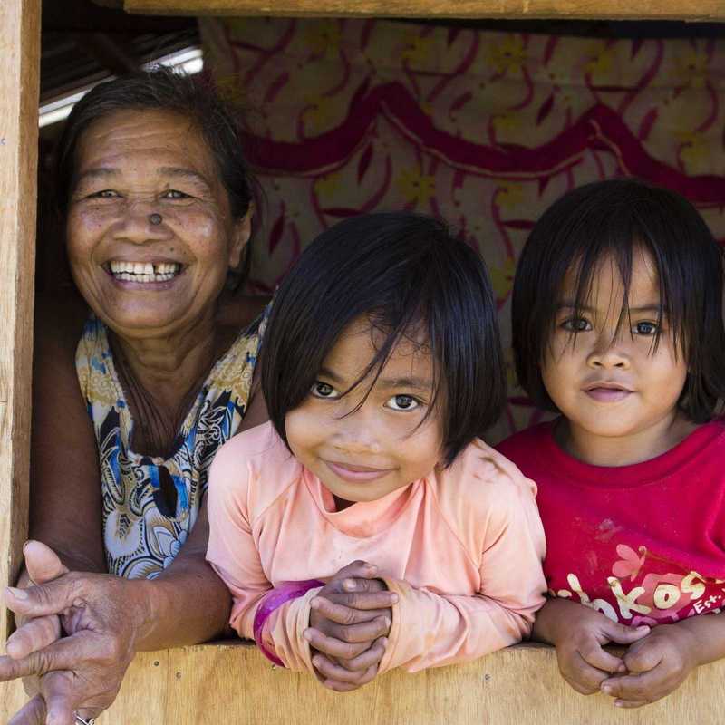 Drei Kinder schauen mit Großmutter aus einem Holzhaus