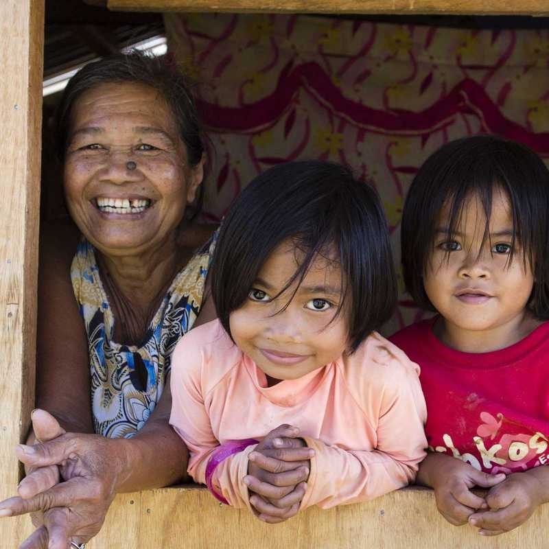 Drei Kinder schauen mit Großmutter aus einem Holzhaus