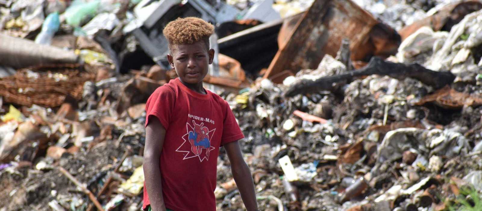 Junge steht vor einem Müllberg